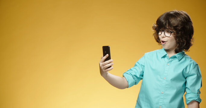 Little cheerful boy using his smartphone when suddenly getting surprised , isolated on yellow background - emotions concept close up 