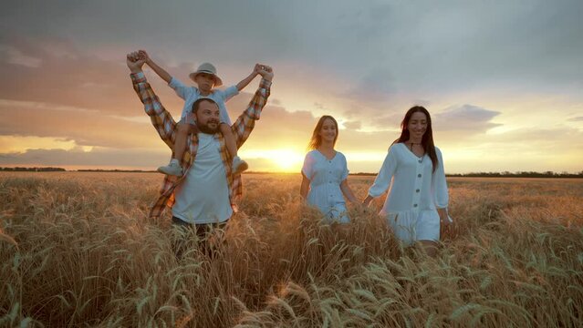 Family Is Resting In Nature In Sunset Or Sunrise Time, Parents And Children Are Running On Golden Field To Bright Sun, Rear View, Peaceful And Happy Life, Mother, Father, Little Son And Teen Daughter