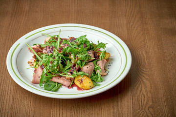 Salad with roast beef, arugula, caramelized onions in a plate on a wooden background