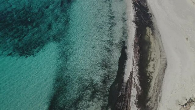 Slow cinematic drone flight over beach with white sand along the coastline of Menorca as waves wash ashore.