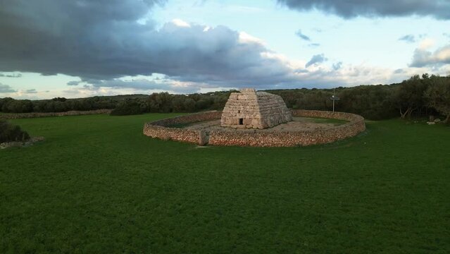 Naveta des Tudons in Menorca, Spain. Drone pans around structure with green grass in the foreground.