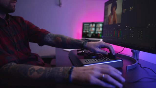 Close-up of a man's hand making edits on a special panel. Young man in glasses working on video editing on computer doing montage and color correction. Concept of creating video content.