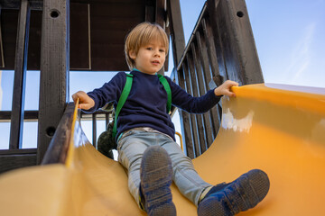 Child playing on outdoor playground. Kids play on school or kindergarten yard. Active kid on colorful slide and swing. Healthy summer activity for children. Little boy climbing outdoors.