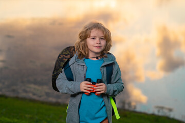 Child with binoculars travelling outdoors. Boy traveler with backpack in a summer day. Portrait of a little boy exploring wildlife. Hiking and adventure concept.