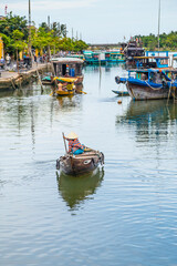Fototapeta na wymiar A small boat being paddled up a river toward larger river boats at Hoi An in Vietnam