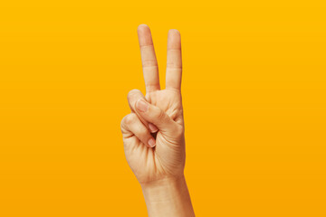 Woman hand showing victory sign on yellow background, two fingers up