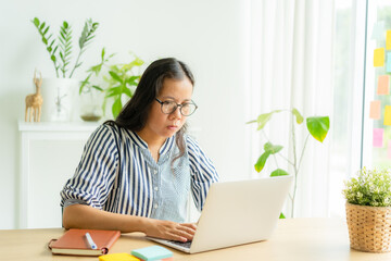 Asian woman using laptop, typing, working at home morning