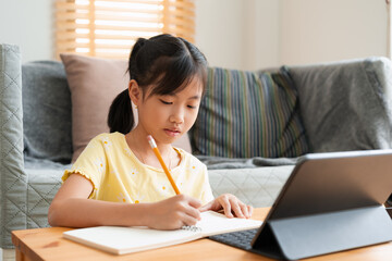 Asian little girl doing homework, learning, student using digital tablet. 
