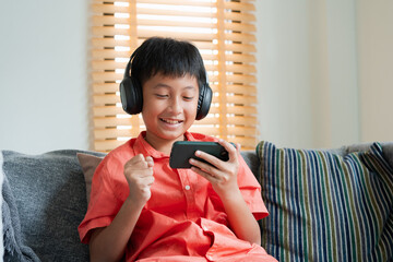 Excited Asian boy playing online game on smart phone with headphones. 