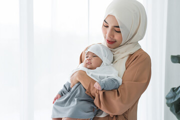 Portrait of Asian Muslim mother wear hijab holding carrying her cute newborn baby 1 month old in...
