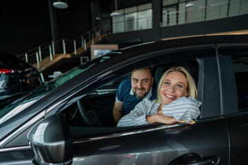 Happy caucasian couple is sitting in a new car in a car dealership.