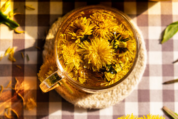 Dandelion flower healthy tea in glass cup on table. Herbal medicine Delicious tisane tea from with fresh yellow blossom dandelion flowers inside tea cup. Green clearing infusion Wildflowers Eco