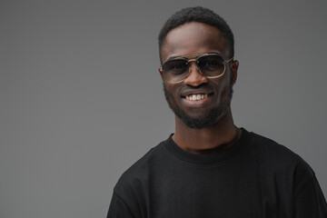 Studio shot of smiling guy of african ethnic dressed in trendy sunglasses and casual attire.