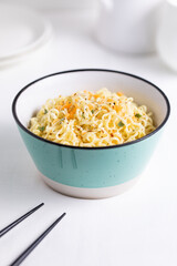 A Turquoise Bowl Filled with Instant Noodles on White and Bright Background 