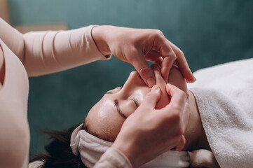 The beautician makes a deep facial massage to a young woman. Face massage technique against aging. Close-up.