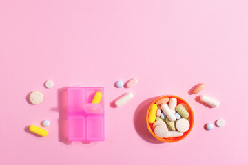 Pharmaceutical medicine pills, tablets, capsules, dietary supplements and pill box on brightly lit pink background with copy space.