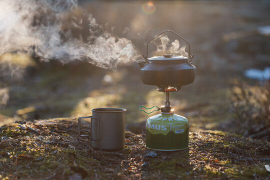 IMATRA, FINLAND - 08 APRIL, 2023: Kettle on gas stove, mug in the spring forest in the evening. Background of the forest is blurred.