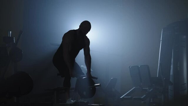 Silhouette of an athlete working on his muscles with weights. Work on your appearance in the gym. High quality 4k footage