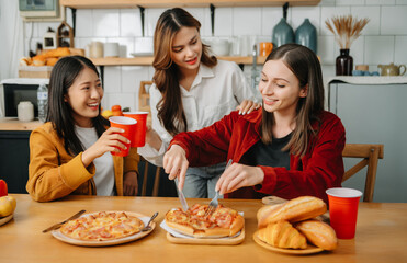 Group of friends making fun at home party.They sitting on desk in living room and eating pizza. .