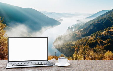 Laptop or notebook, blank screen, placed on a wooden table, black coffee in a white coffee mug. complex mountain morning sun During the sunrise. Travel concept .3D Rendering