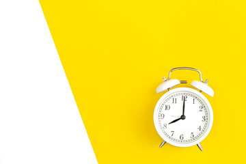 White alarm clock on a white and yellow background, flat lay.