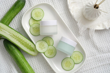 Obraz na płótnie Canvas Cream jars unlabeled and cucumber slices on white fabric background. Mockup for cosmetic of cucumber extract. The high water content and antioxidants in cucumber make the skin supple and elastic.