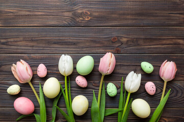 Happy Easter composition. Easter eggs on colored table with yellow Tulips. Natural dyed colorful eggs background top view with copy space