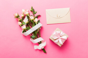 Greeting card mockup with copy space, pink ribbon and roses flowers on colored table background. Flat lay, top view. mother day holiday concept