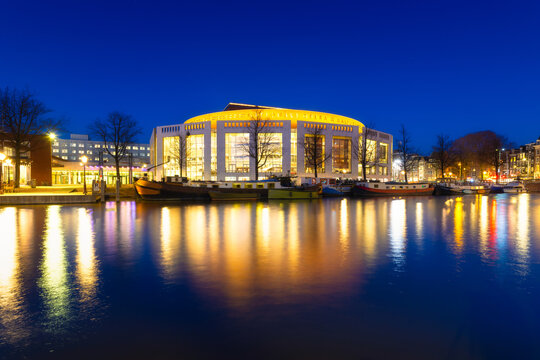 Amsterdam, Netherlands. Opera and Ballet Building. Evening cityscape. Blue sky and city lights.  Dutch canals. Reflections on the surface of the water. Photography for design and wallpaper.