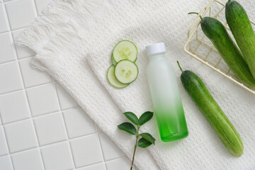 A gradient white and green bottle decorated with Cucumber slices and green leaves on a towel. Cucumber (Cucumis sativus) helps disappear dark circles and dark spots