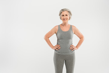 happy senior woman in tank top standing with hands on hips isolated on grey.