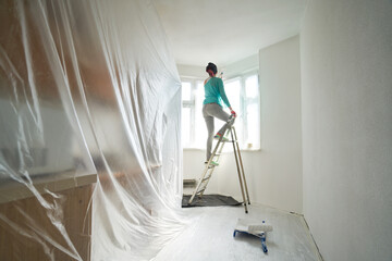 Woman stands on the stairs and paints the wall with a roller