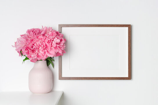 Blank landscape frame mockup on white wall with fresh flowers