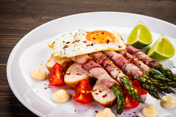 Sunny side up egg and asparagus wrapped in bacon on wooden background
