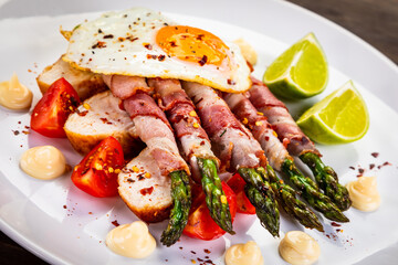 Sunny side up egg and asparagus wrapped in bacon on wooden background
