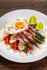 Sunny side up egg and asparagus wrapped in bacon on wooden background
