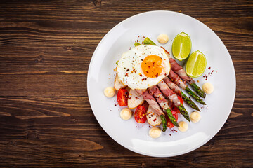 Sunny side up egg and asparagus wrapped in bacon on wooden background
