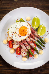 Sunny side up egg and asparagus wrapped in bacon on wooden background
