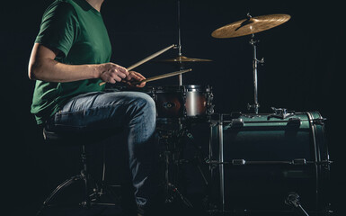 A man plays a drum kit on a black background.