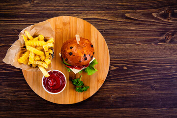 Big cheeseburger with French fries on wooden board