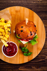 Big cheeseburger with French fries on wooden board