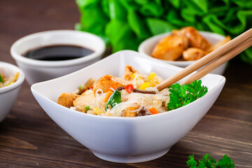 Asian food - chicken nuggets, rice noodles, stir fried vegetables, soy sauce and mushrooms on wooden table 