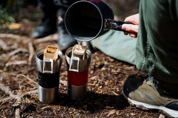 A tourist brews coffee in nature, pour boiling water into the filter bag for coffee, a thermal mug for hot drinks, a paper filter on a hike.