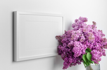 Landscape picture frame mockup on whte wall with fresh lilac flowers bouquet, blank mockup with copy space