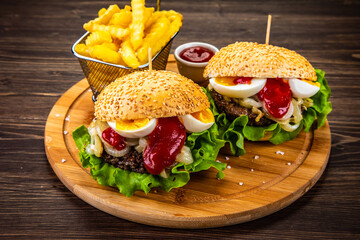Big hamburgers with boiled egg and French fries on wooden board
