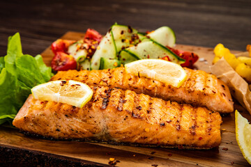 Fried salmon steak with French fries and fresh vegetable salad served on wooden table
