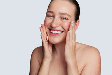 Optimistic young woman applying facial cream during skincare procedure