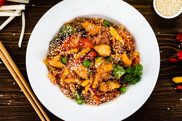 Asian food - chicken nuggets, rice noodles, stir fried vegetables, soy sauce and mushrooms on wooden table

