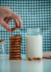 Fotobehang Closeup of tasty cookies with a jar of milk on the table on blue background © George Fallon/Wirestock Creators