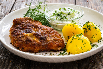 Breaded fried pork chop with fresh cucumber in cream and potatoes on wooden table 